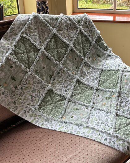 small cotton flannel rag quilt with a llama theme thrown over a settee with a wooden frame and upholstered in a small print dusty rose velvet fabric